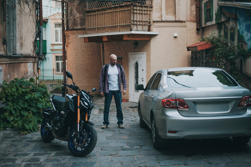 Man Standing Between a Car and a Motorcycle
